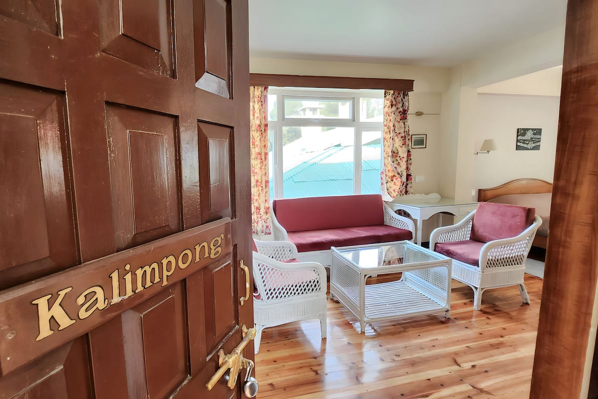 Quarto com porta de madeira identificada como "Kalimpong", mobiliário de vime branco, um sofá vermelho e uma pequena mesa.