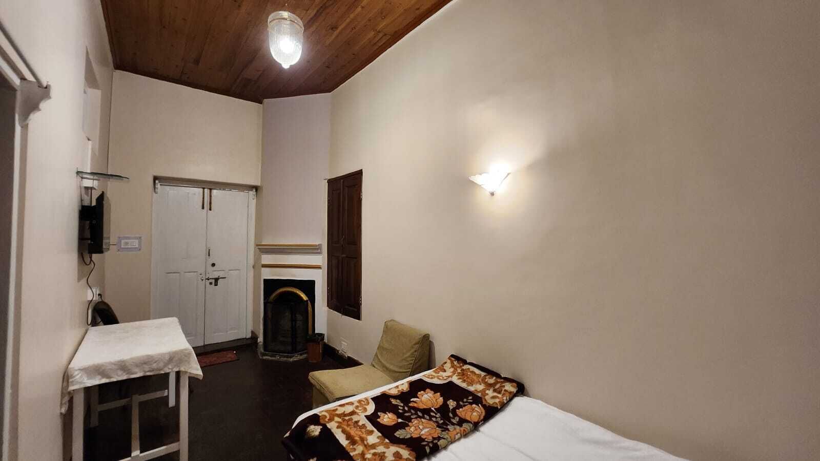 A room with a bed, a small table, a chair, a fireplace, and a door.