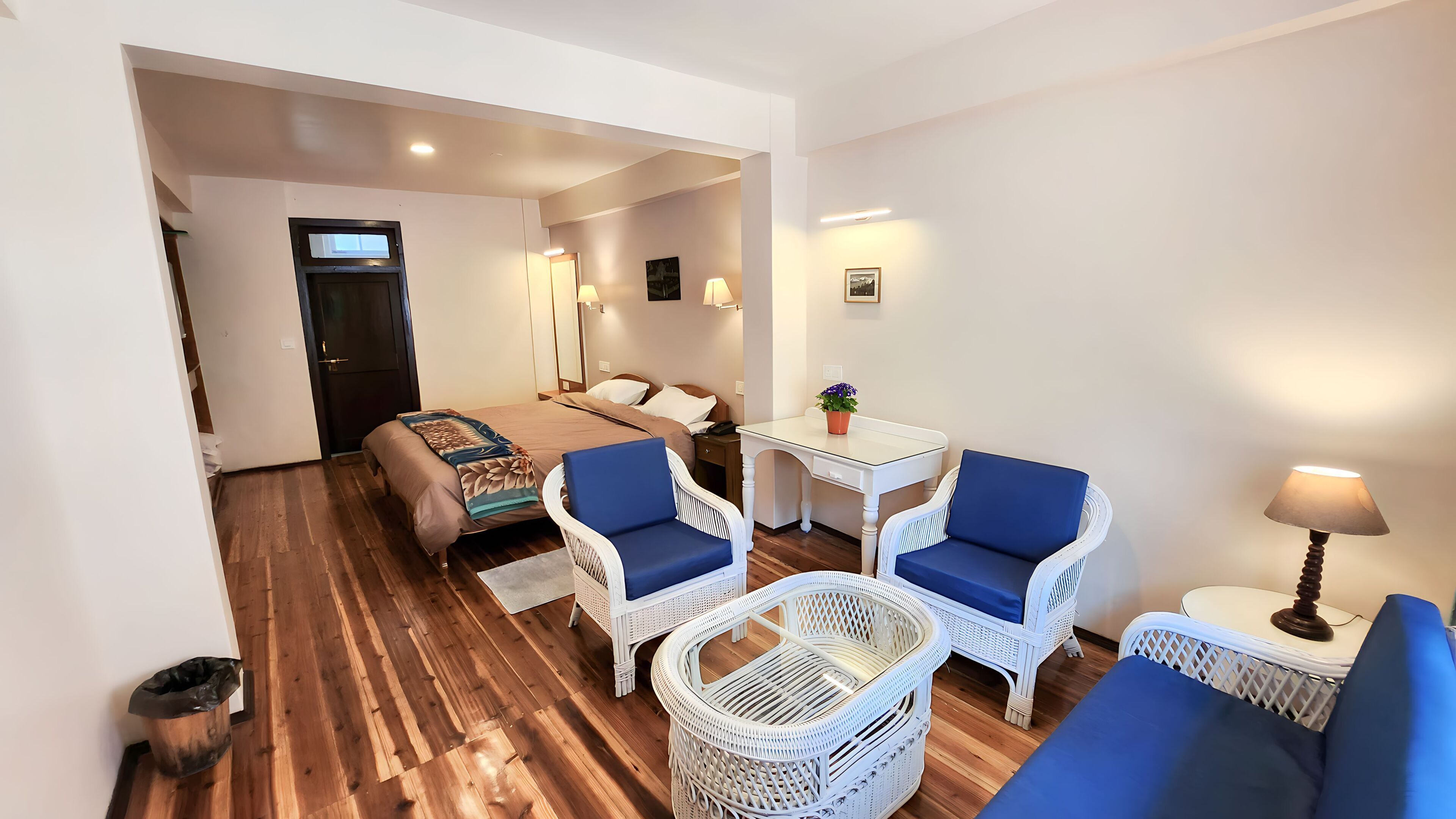 A hotel room with a bed, two blue chairs, a white table, and a lamp.