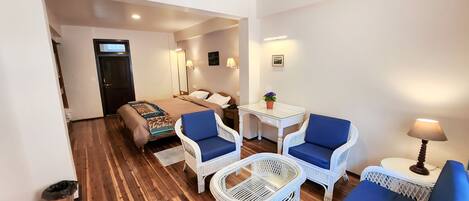 A hotel room with a bed, two blue chairs, a white table, and a lamp.
