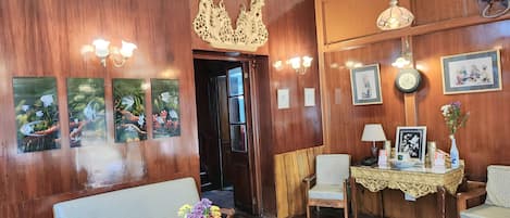 A wooden-finished room with a sofa, a dining table with chairs, wall-mounted artwork, and a decorative ceiling piece.