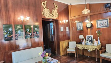 A wooden-finished room with a sofa, a dining table with chairs, wall-mounted artwork, and a decorative ceiling piece.