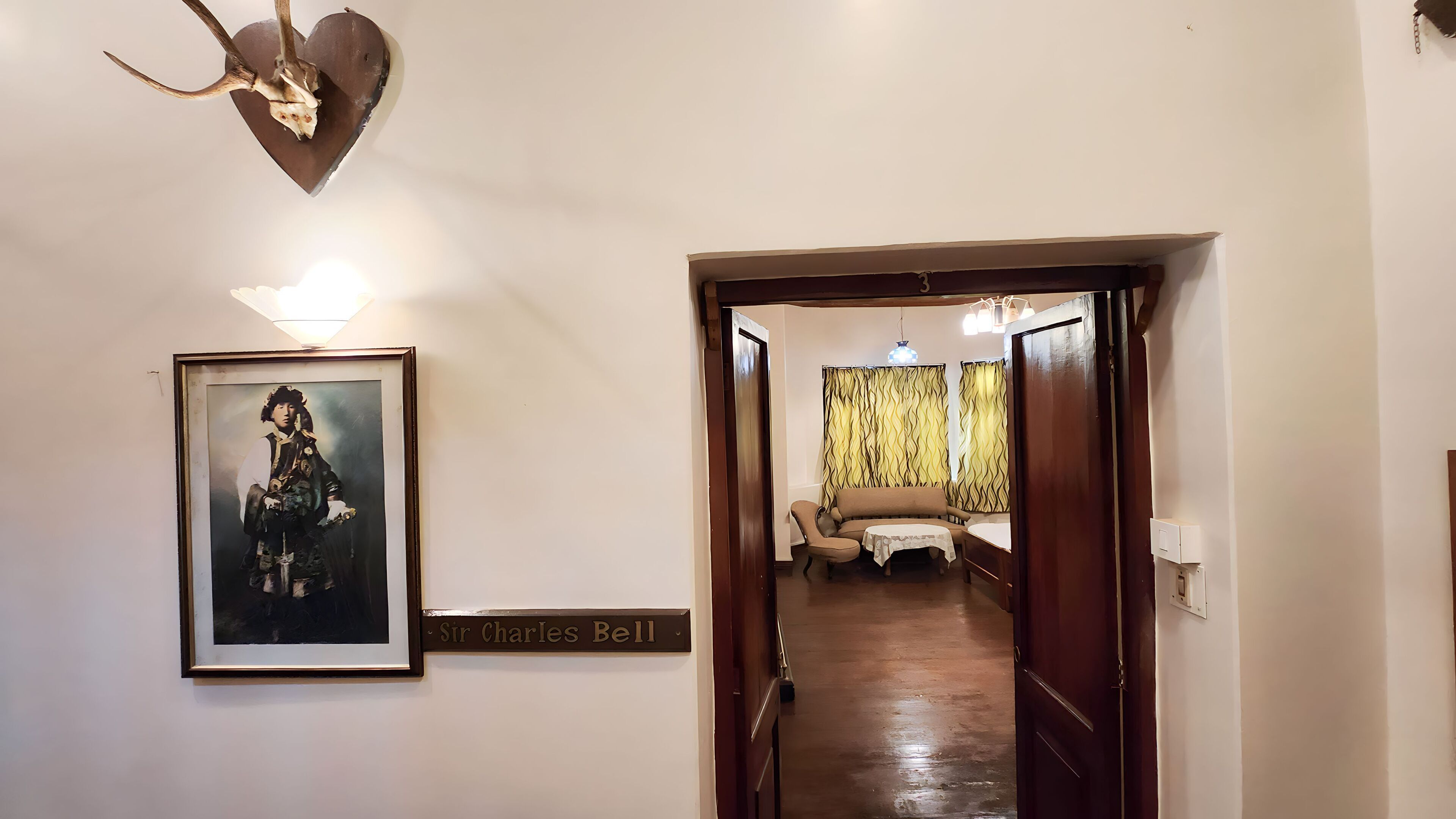 A hallway with a framed portrait, a nameplate reading "Sir Charles Bell," and a wooden door leading to a room with a sofa and a table.