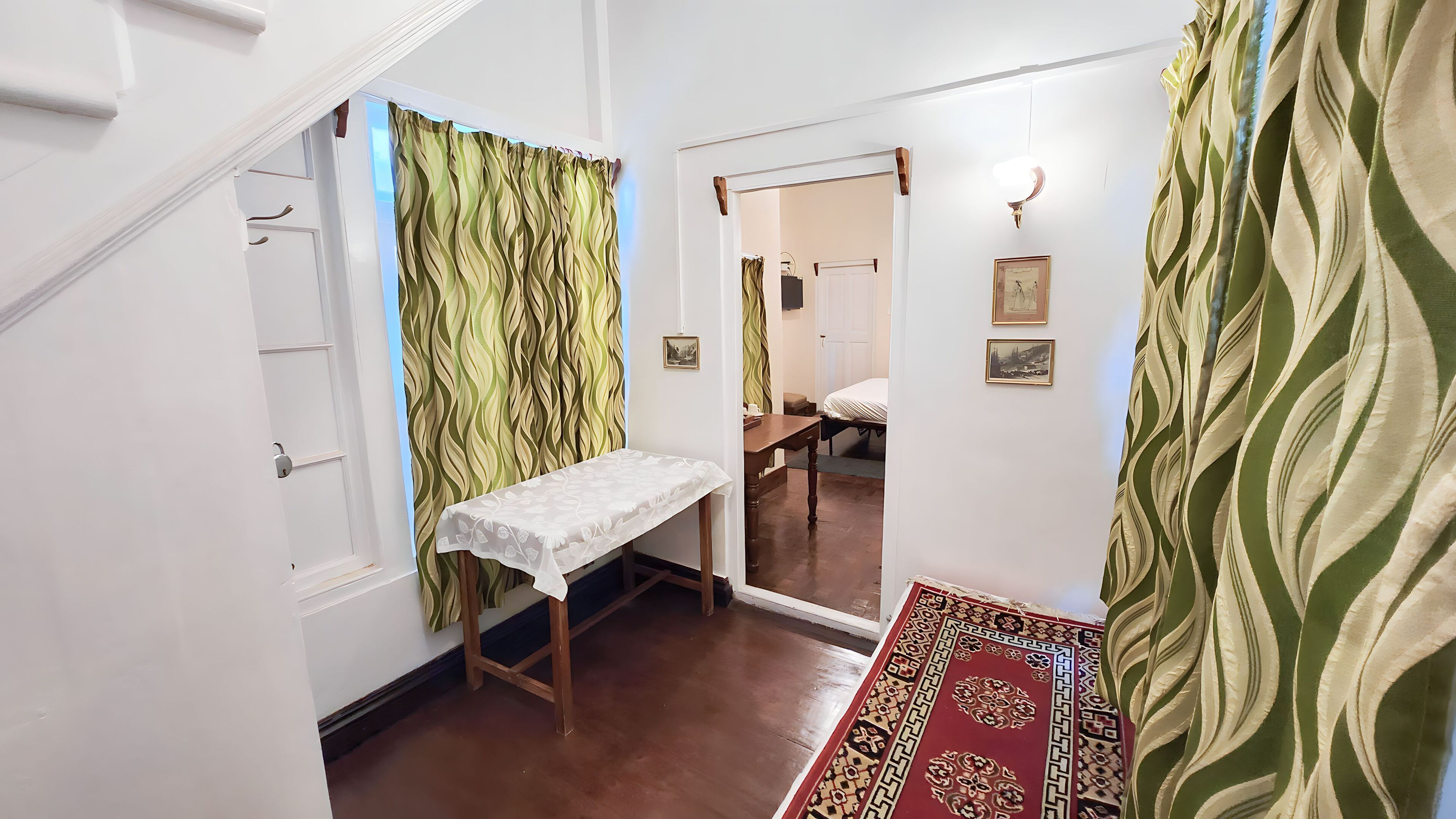 Quarto com uma cama, uma mesa com toalha branca, um tapete estampado e um espelho na parede.