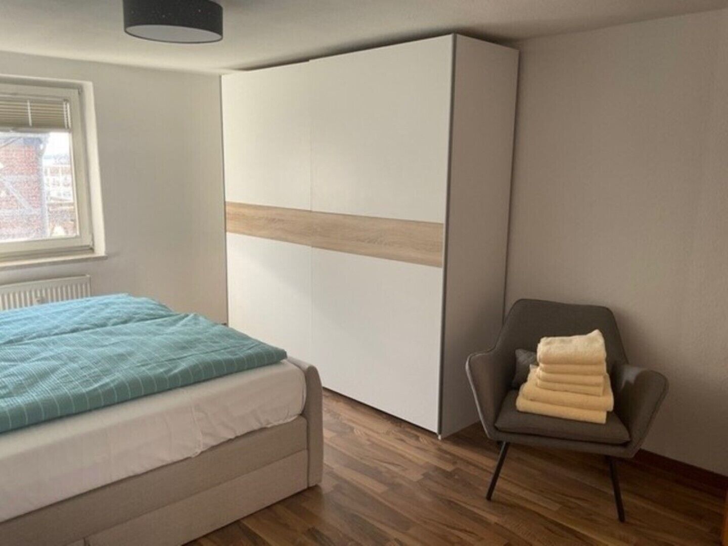 A bedroom with a bed, a wardrobe, a chair, and a window.
