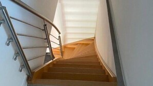 A staircase with a metal handrail and wooden steps leading to a landing with a white ceiling. - Vacation apartment 10 lake view (Sellin)