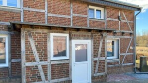 A two-story brick building with a white door and windows, a visible number '126', and a brick pathway leading to a gate. - Vacation apartment 10 lake view (Sellin)