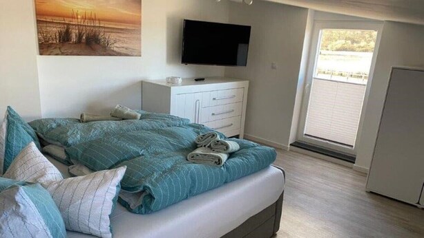 A bedroom with a bed, a TV, a dresser, and a window. - Vacation apartment 10 lake view (Sellin)