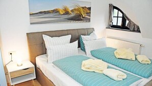 A double bed with two pillows, a bedside table with a lamp, and a window with curtains. - Ferienwohnung 6 Jasmund (Sellin)