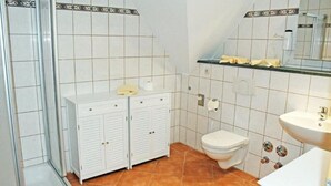 A bathroom with white lockers, a toilet, a sink, and a shower area. - Ferienwohnung 6 Jasmund (Sellin)