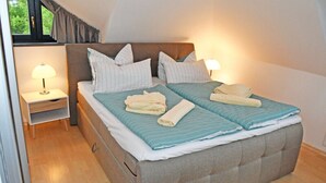 Cama doble con ropa de cama a rayas, dos almohadas y toallas dobladas. Se ve una mesita de noche con una lámpara y un mueble con un cajón.