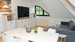 Un moderno salón con una mesa de comedor blanca, sillas blancas, un sofá gris y un televisor.