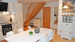 Una cocina moderna con armarios blancos, horno empotrado y comedor con mesa y sillas blancas.