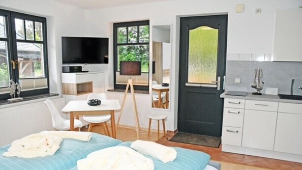 Un dormitorio con cama, escritorio, silla, televisor y una zona de cocina.