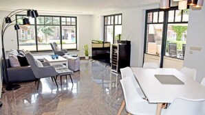 Uma sala de estar moderna com sofá, mesa de jantar e cadeiras, janelas amplas e lareira.
