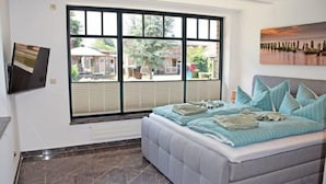 Quarto com uma janela grande, uma cama com várias almofadas e um quadro na parede.