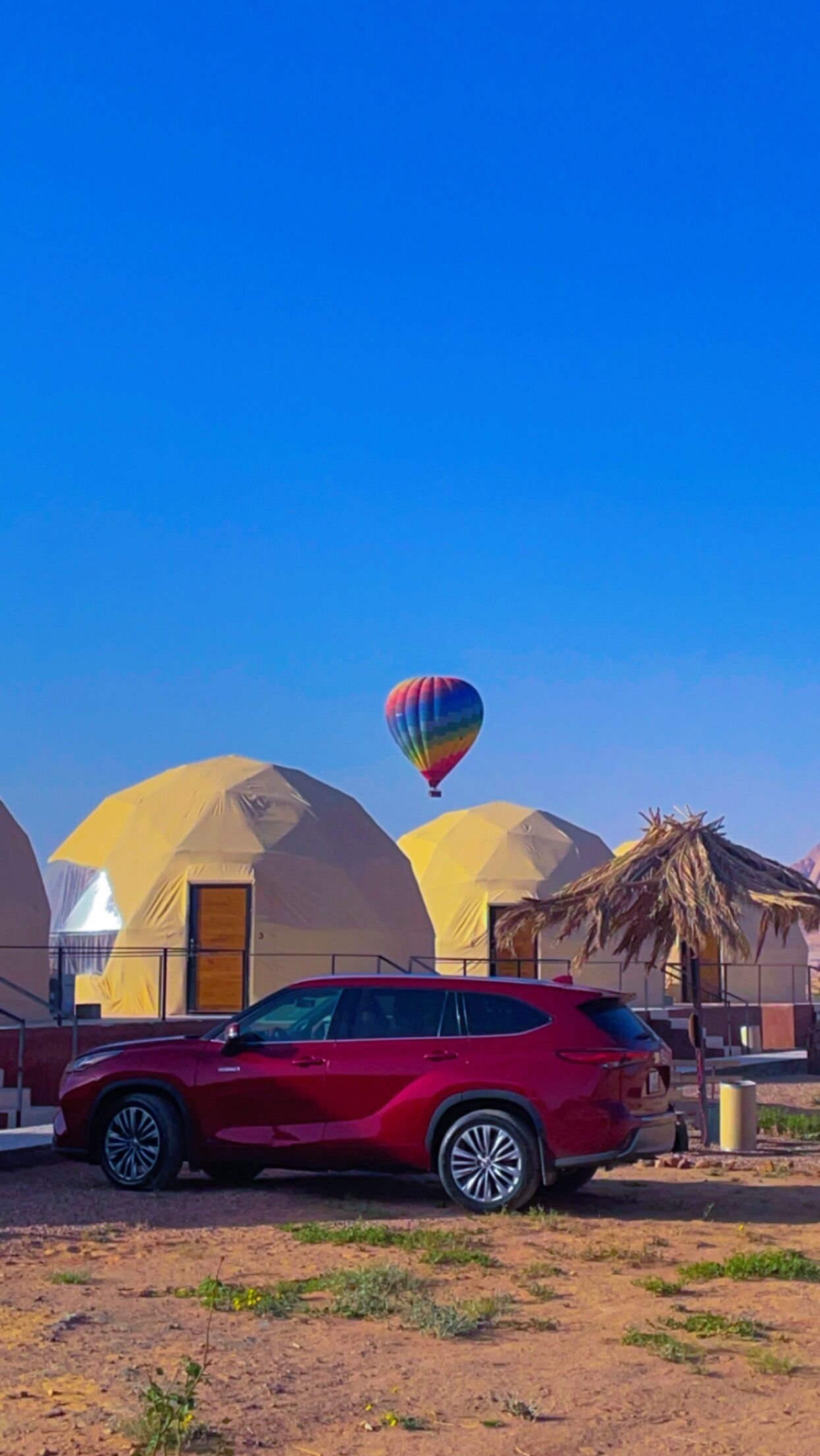 A red SUV parked in front of yellow dome-shaped buildings with a hot air balloon in the sky.