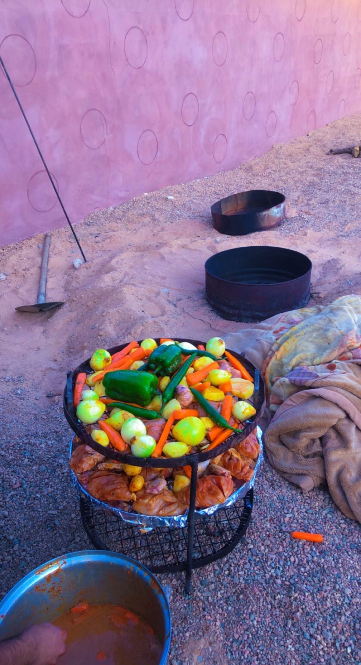 Een barbecue met diverse groenten en vlees, een schep en een pan saus op een grindpad.