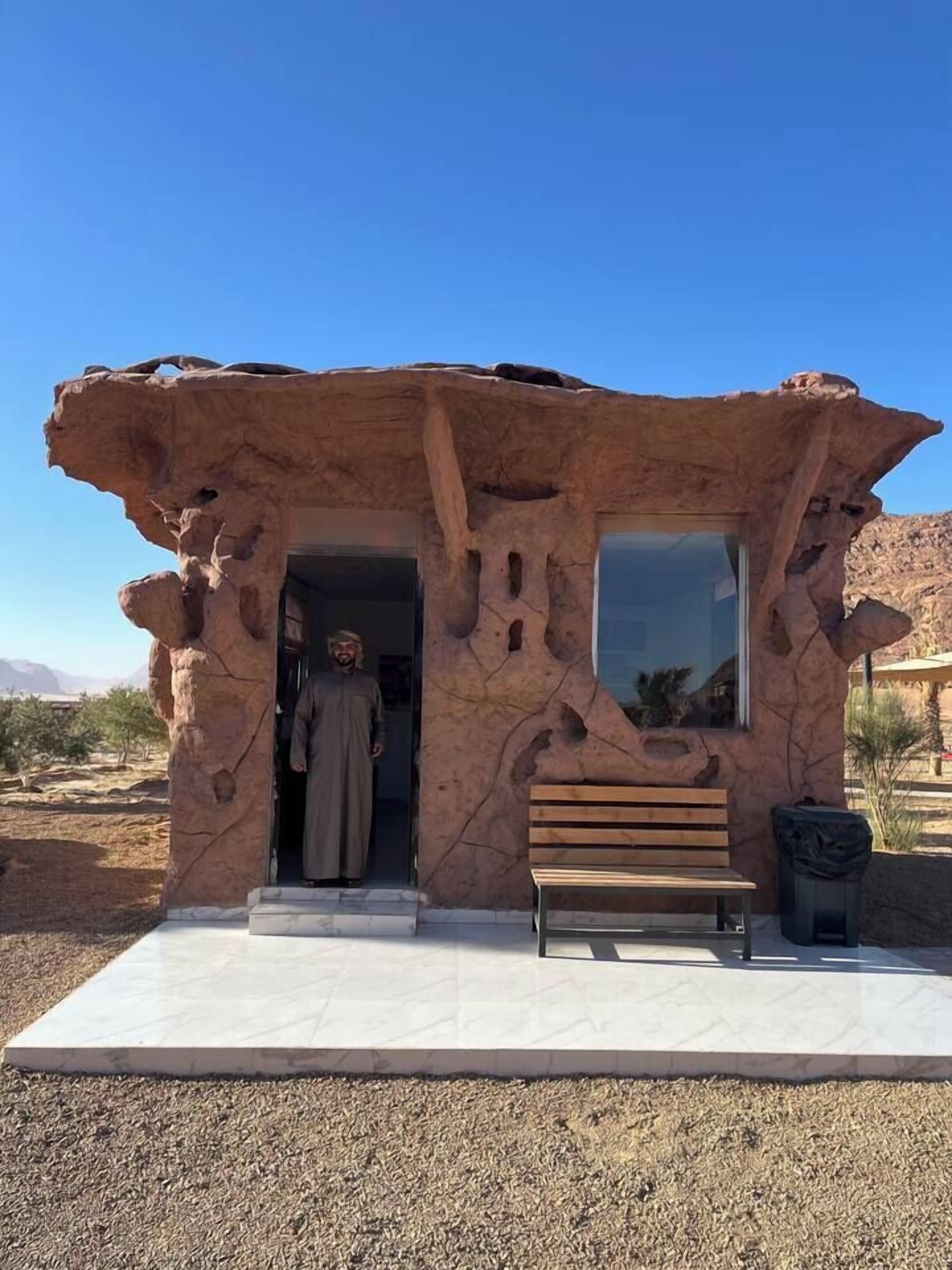 A rock-like structure with a bench and a trash bin in front.