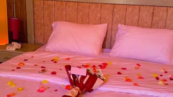 Una habitación de hotel con cabecera de madera, una cama con ropa de cama rosa y un ramo de flores sobre la cama.