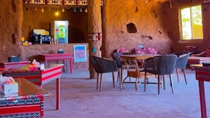 An interior with a rustic cave-like ceiling, a dining area with tables and chairs, and a refrigerator in the background. - Adel rum camp  (Wadi Rum)