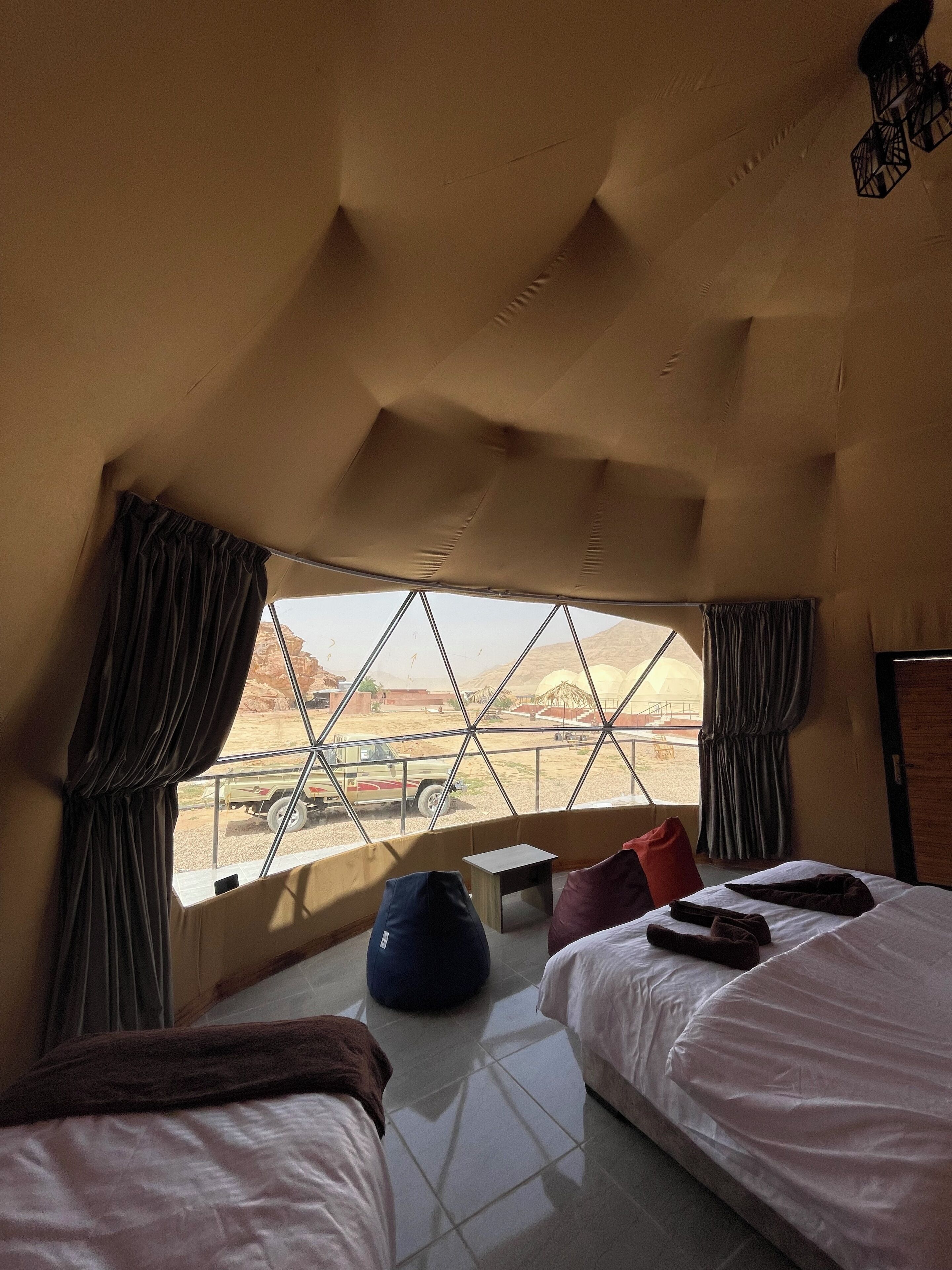 Une chambre avec deux lits, une petite table et une vue sur un paysage désertique, visible à travers une grande fenêtre.