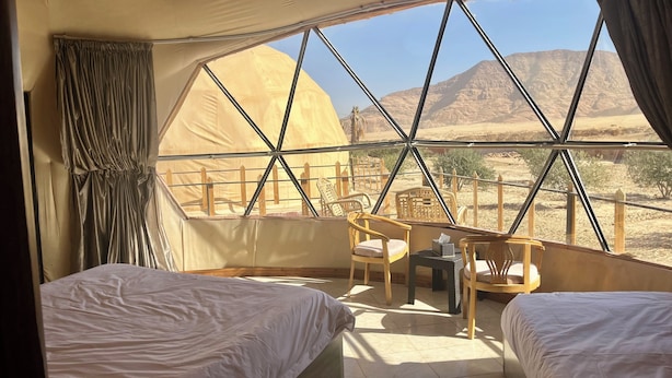 A room with two beds, a small table, and chairs, with a view of desert mountains through large windows. - Adel rum camp  (Wadi Rum)