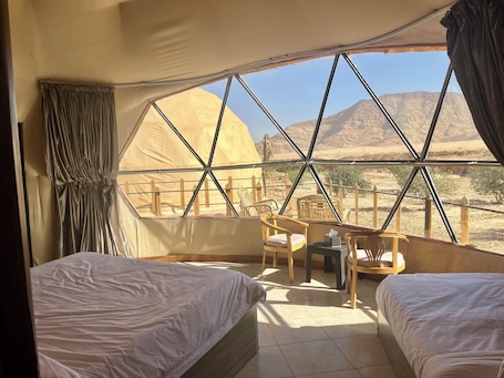 A room with two beds, a small table, and chairs, with a view of desert mountains through large windows.