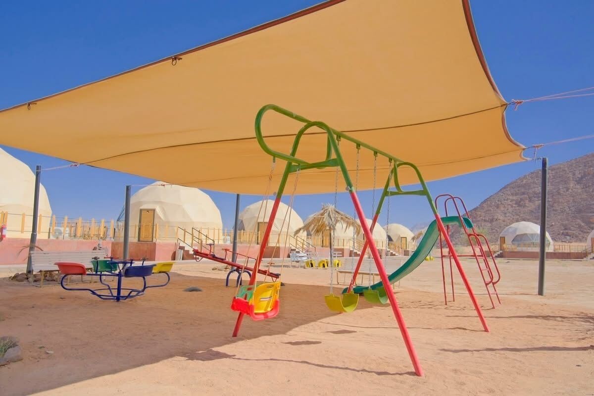 A playground with swings and slides, a picnic table, and a shaded area.
