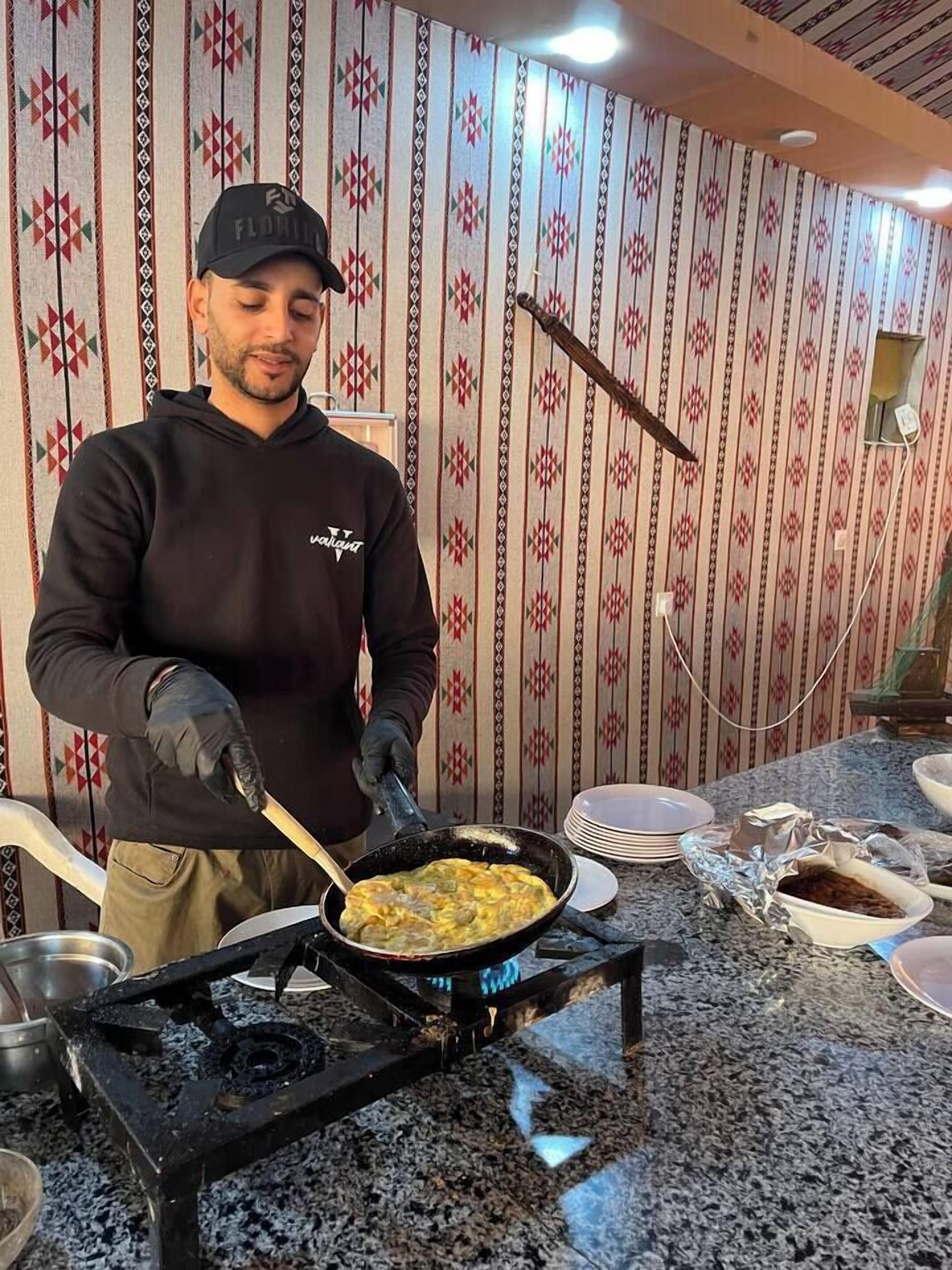A person cooking on a portable stove in a room with patterned wallpaper.