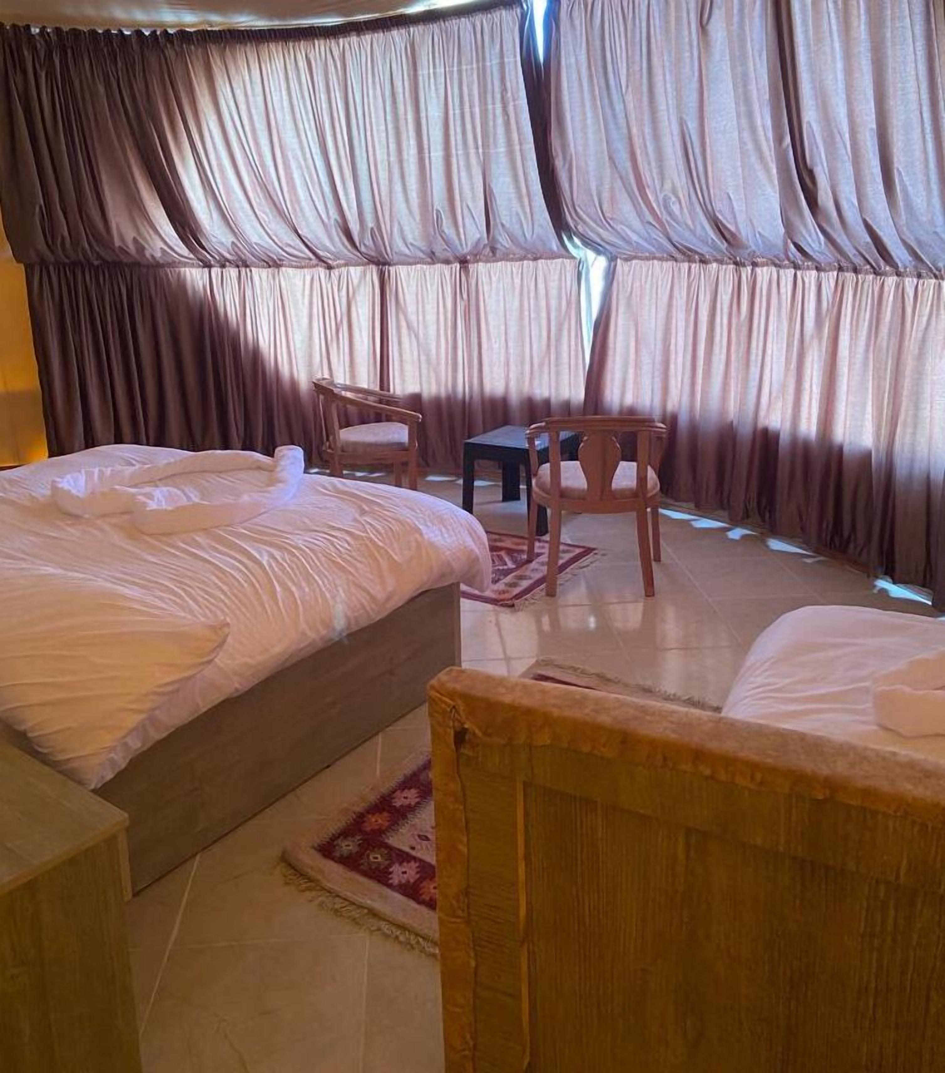 Una camera da letto con due letti, una sedia di legno, un tavolino e un tappeto decorato.