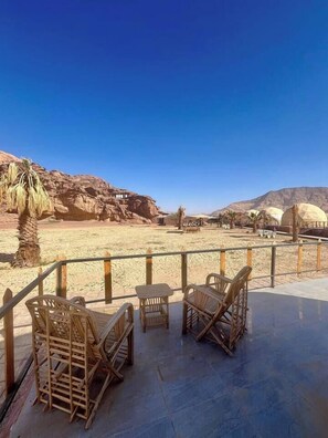 A terrace with wicker furniture overlooking a desert landscape with rock formations and domed structures. - Adel rum camp  (Wadi Rum)