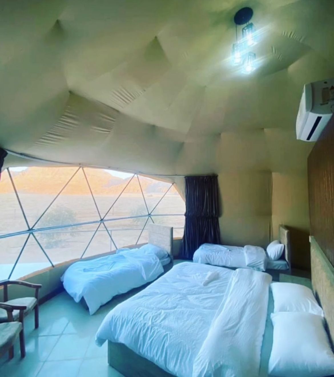 A room with three beds, a window with a view of the landscape, and a ceiling fan.