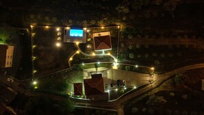 An aerial view of a well-lit, landscaped area with a central building, pathways, and a parking lot. - Uphill Glavanovic Pool Villa (Bar)