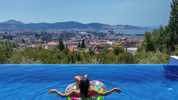 A person floating on a pool with a view of a cityscape and hills in the background. - Uphill Glavanovic Pool Villa (Bar)