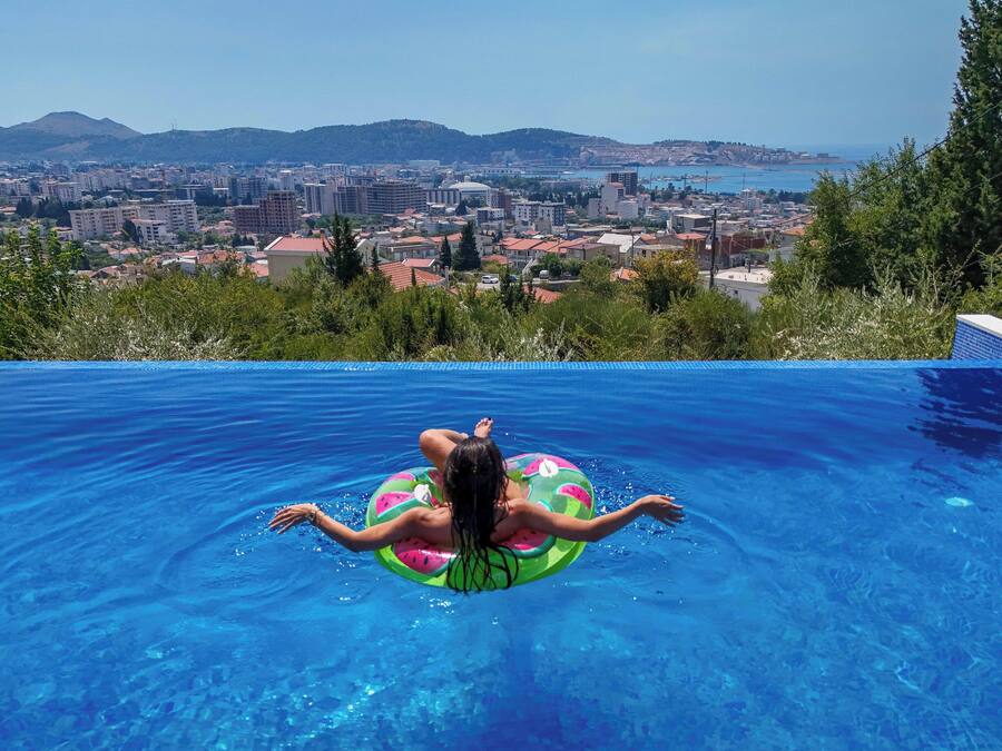 A person floating on a pool with a view of a cityscape and hills in the background.