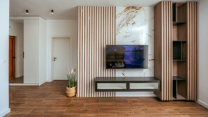 Una sala de estar moderna con un televisor de pantalla plana montado en una pared con paneles de madera verticales. Hay un banco empotrado debajo del televisor y una planta pequeña en el suelo.