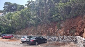 A parking area with cars parked near a stone wall and a hillside. - Agape Rose (Klinci)