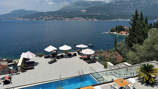 A poolside area with lounge chairs and umbrellas, overlooking a lake with boats and a distant cityscape. - Agape Rose (Klinci)