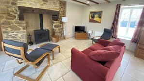 Una sala de estar acogedora con chimenea de piedra, un sofá rojo, sillas de madera y un televisor.