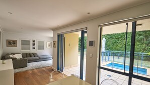 Una sala de estar moderna con un sofá, una mesa de comedor y vistas a una piscina a través de amplios ventanales.