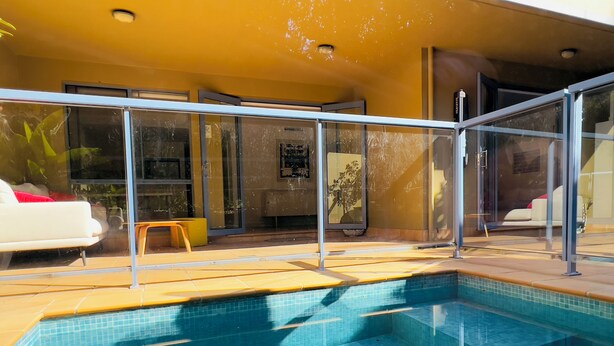 Una piscina con barandillas de cristal, un sofá blanco y una silla amarilla.