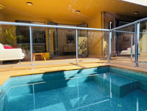 Une piscine avec des rampes en verre, un canapé blanc et un fauteuil jaune.