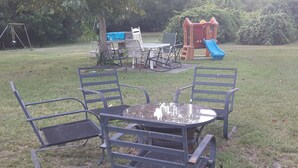 A grassy outdoor area with a metal table and four chairs, a swing set, and a play structure with a slide. - Private, 1 Mile to Poe, 4 miles to Blue, 6 Miles to Ginnie. Tent/Camper camping (High Springs)