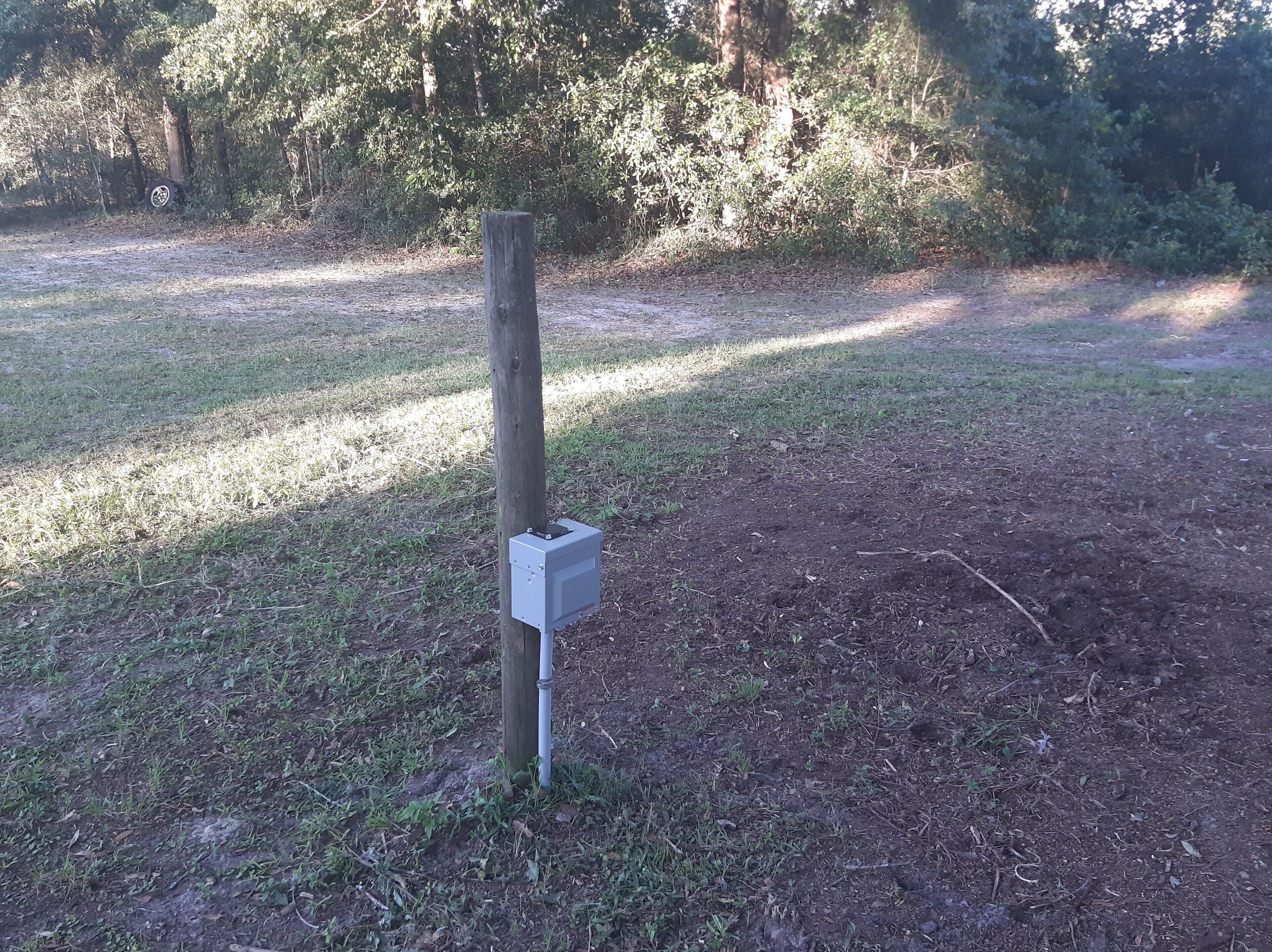 A utility box mounted on a wooden post in a grassy area with trees in the background.