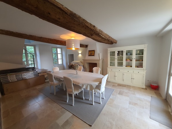 A dining area with a white table and chairs, a wooden ceiling beam, and a cabinet with glass doors.