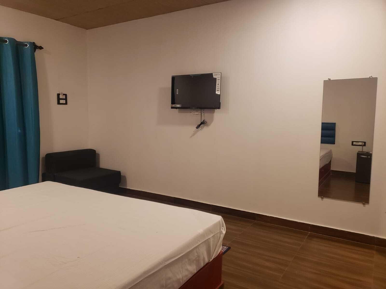 Une chambre d’hôtel avec un lit, un téléviseur fixé au mur, un miroir, une petite table et un rideau bleu.