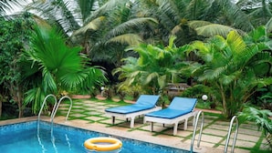 A pool area with two lounge chairs and a floating ring, surrounded by lush greenery and palm trees. - White Truffle Resort (Arambol)