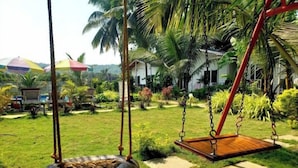 A garden with a swing set, palm trees, and a tire swing. - White Truffle Resort (Arambol)