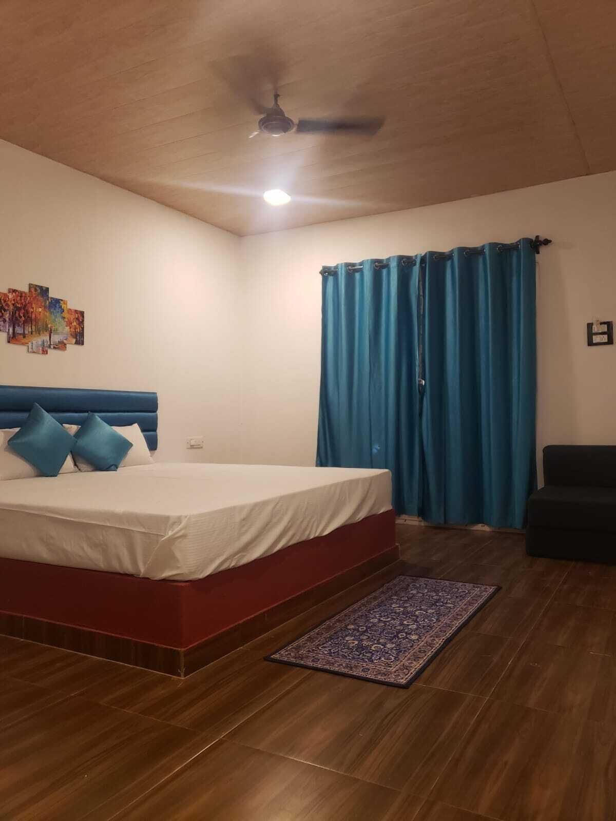 Un dormitorio con cama, ventilador de techo, cortina azul y una alfombra pequeña.